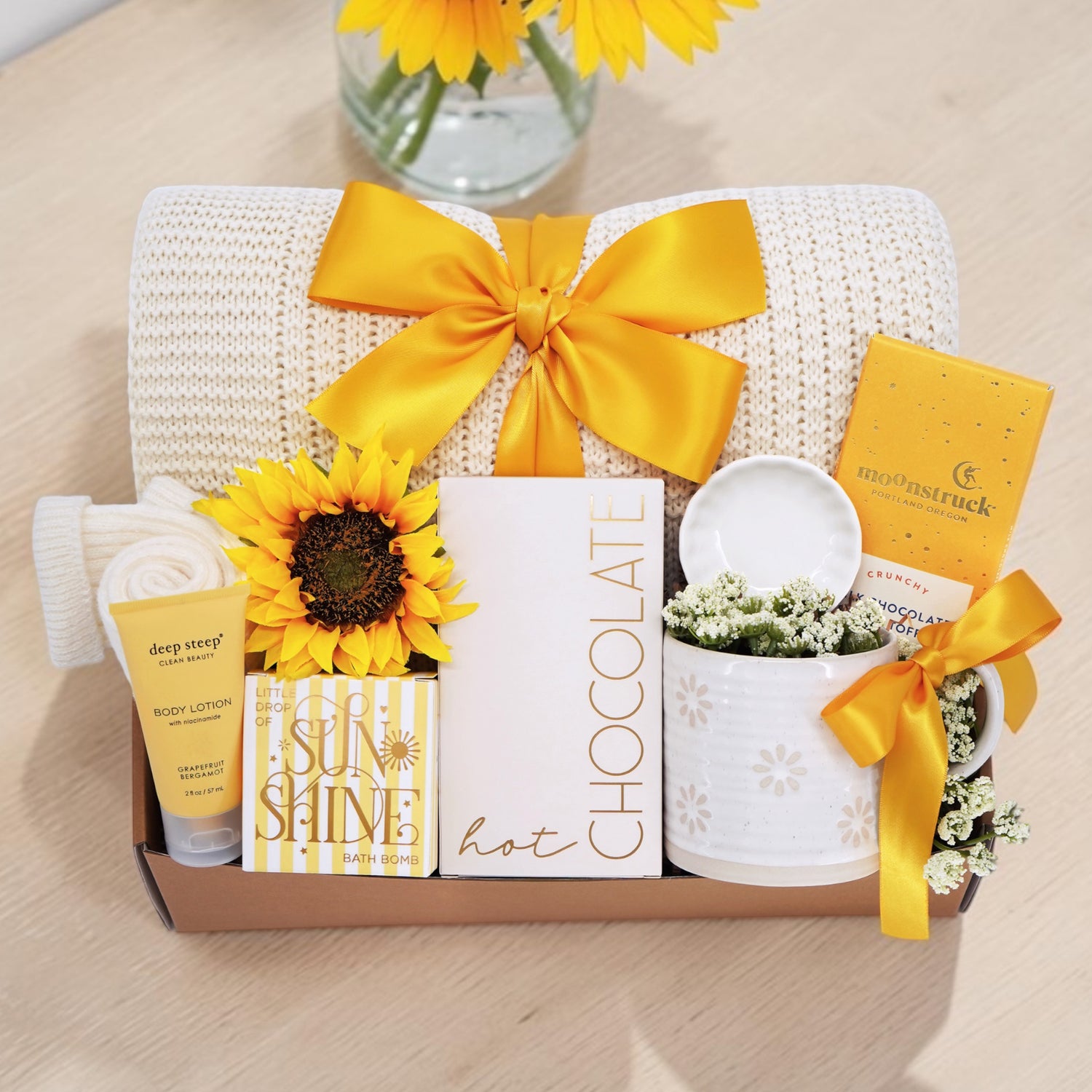 Wildflower Pop Sunny Days Ahead blanket gift box with a cream lace knit blanket, Wildflower Pop daisy ceramic mug, scallop trinket dish, moonstruck milk chocolate and toffee bar, little drop of sunshine bath bomb, faux sunflower, deep steep lotion, and cream knit socks