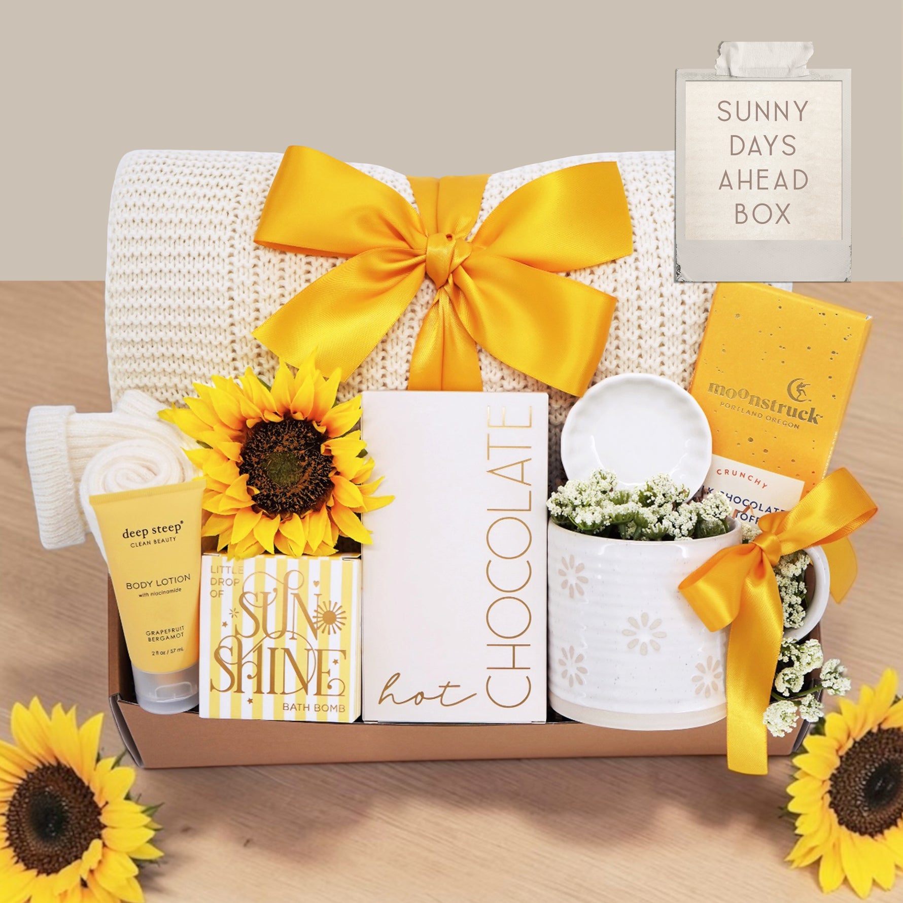 Wildflower Pop Sunny Days Ahead blanket gift box with a cream lace knit blanket, Wildflower Pop daisy ceramic mug, scallop trinket dish, moonstruck milk chocolate and toffee bar, little drop of sunshine bath bomb, faux sunflower, deep steep lotion, and cream knit socks