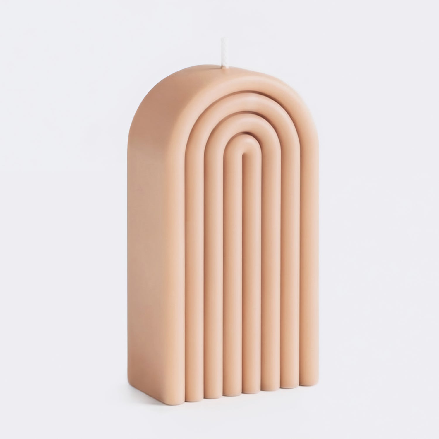 A candle with a ribbed, arch-shaped design in a warm peach-beige color, photographed on a clean light gray background.