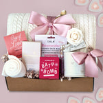 Wildflower Pop Gift box with cable knit blanket,  bath products including a bath bomb, face mask, and tea on a pink background.