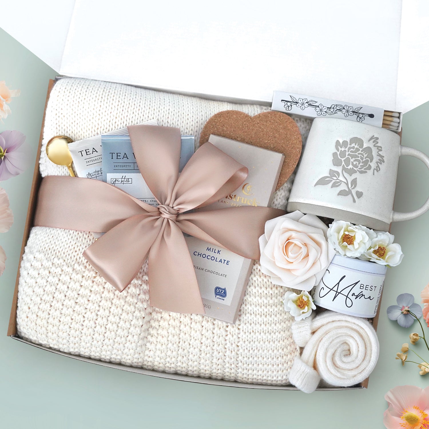 The best mama blanket box comes with a cream lace knit blanket tied in a nude ribbon, 2 tea with tea tea bags, gold demitasse spoon, heart coaster, full size Moonstruck milk chocolate bar, 4" box of matches, mama peony ceramic mug, best mama soy wax candle, cream knit socks, faux forever rose 
