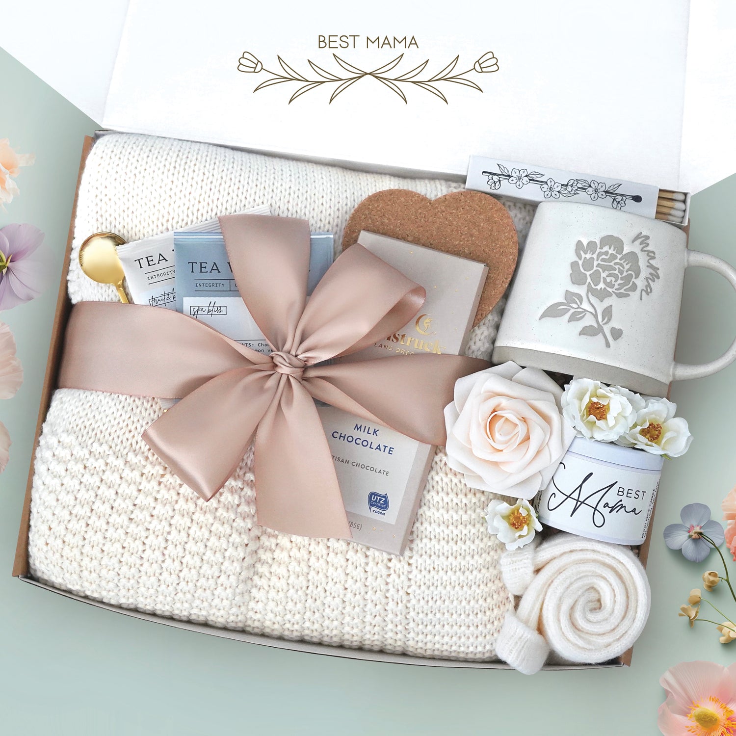 The best mama blanket box comes with a cream lace knit blanket tied in a nude ribbon, 2 tea with tea tea bags, gold demitasse spoon, heart coaster, full size Moonstruck milk chocolate bar, 4" box of matches, mama peony ceramic mug, best mama soy wax candle, cream knit socks, faux forever rose 