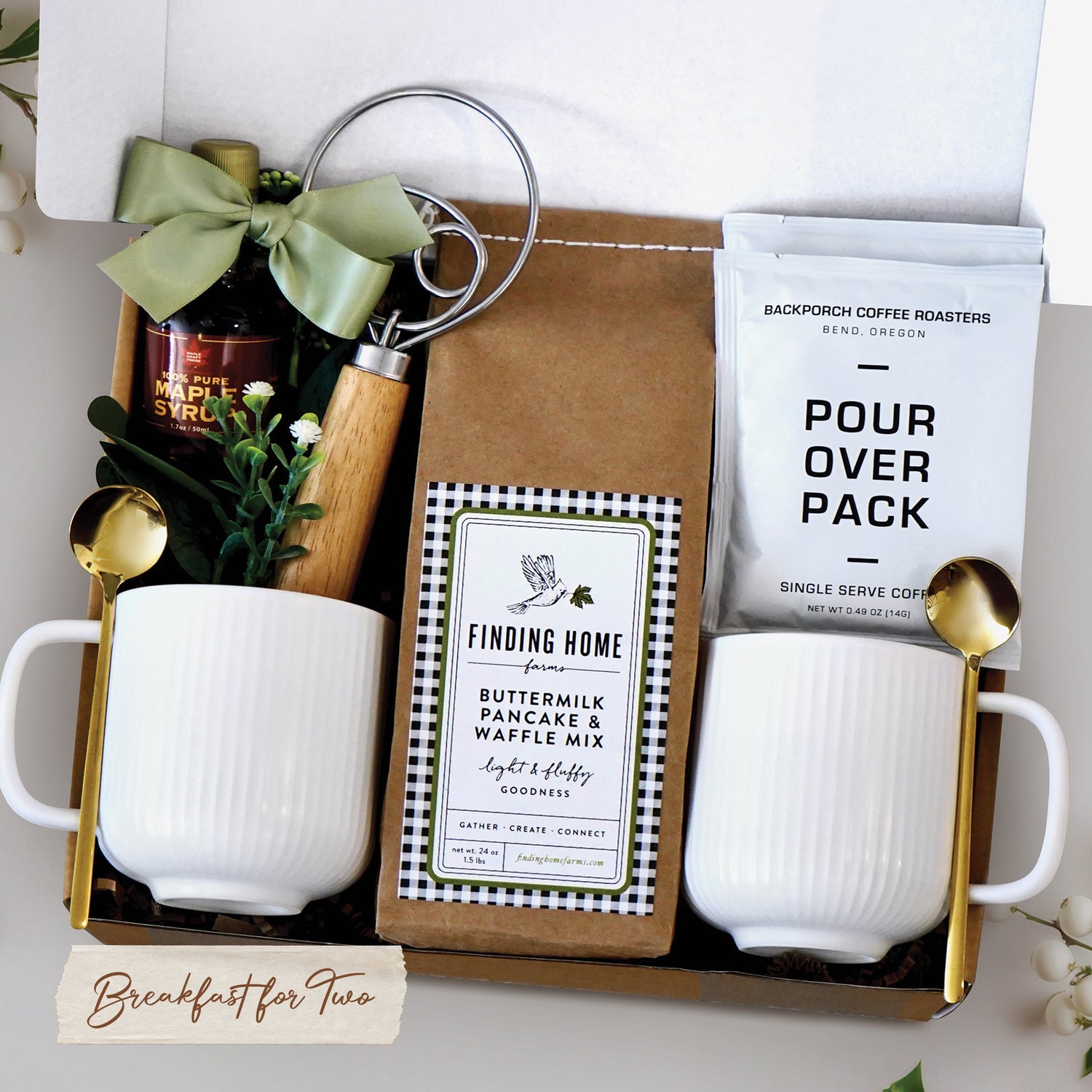 Breakfast for Two Gift Box for Couples includes 2 ceramic white ribbed mugs, 2 gold spoons, 1 dough whisk, 1 1.7oz maple syrup, 2 single serve coffee packs, and one 24oz pancake and waffle mix