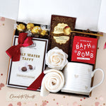 Chocolate Heart Gift Box comes with a rustic heart ceramic mug, gold demitasse spoon, Seaberry and Rose Bath Bomb, cream knit socks, chocolate salt water taffy, chocolate truffles, chocolate truffle hot cocoa mix, and a faux rose head
