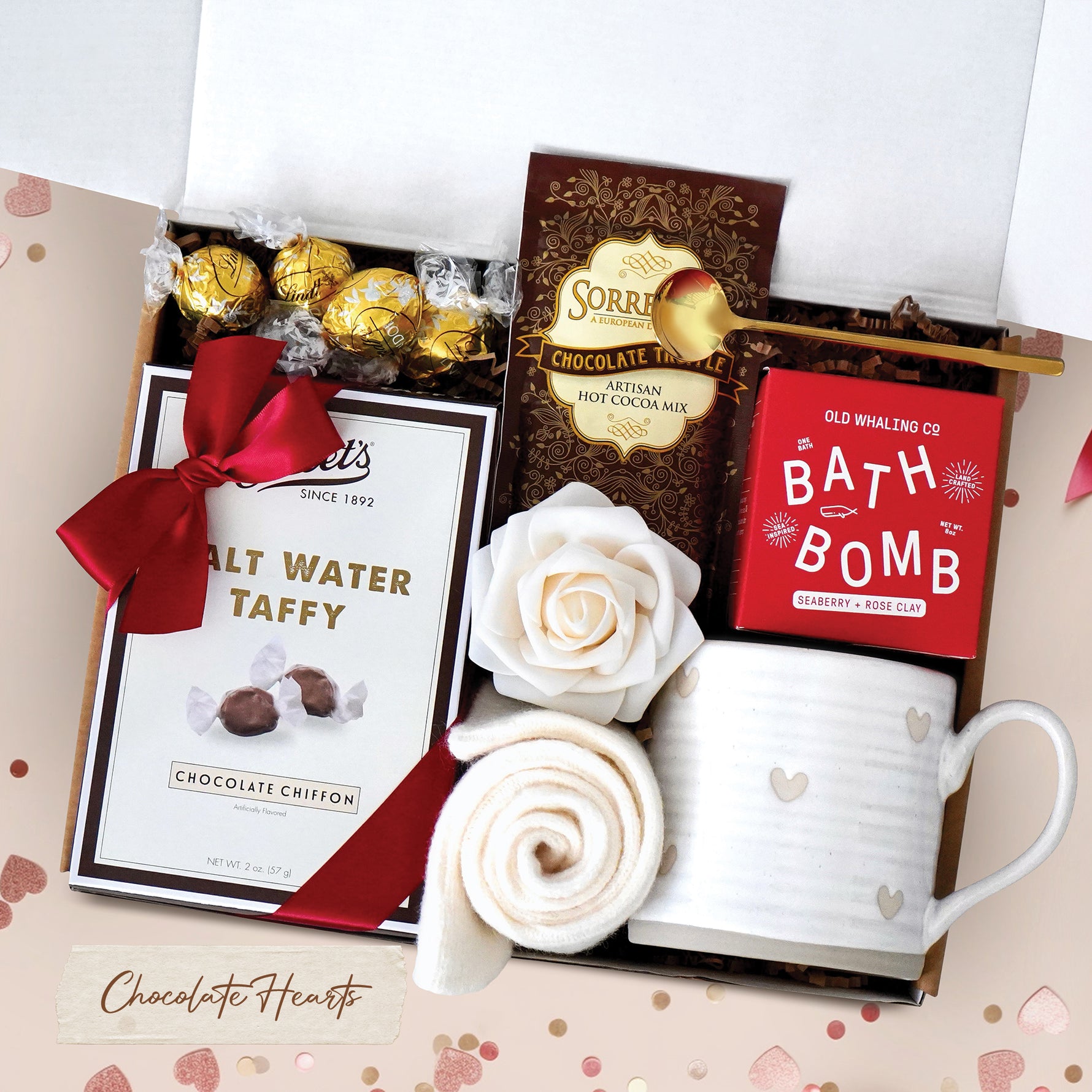 Chocolate Heart Gift Box comes with a rustic heart ceramic mug, gold demitasse spoon, Seaberry and Rose Bath Bomb, cream knit socks, chocolate salt water taffy, chocolate truffles, chocolate truffle hot cocoa mix, and a faux rose head