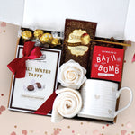 Chocolate Heart Gift Box comes with a rustic heart ceramic mug, gold demitasse spoon, Seaberry and Rose Bath Bomb, cream knit socks, chocolate salt water taffy, chocolate truffles, chocolate truffle hot cocoa mix, and a faux rose head