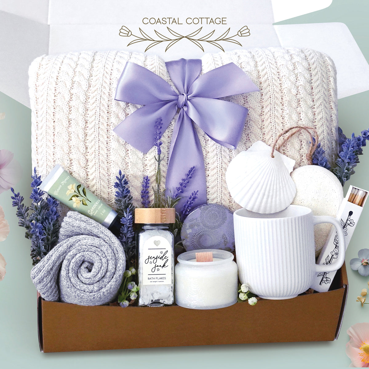 The Costal Cottage comes with a cream cable knit blanket tied with a lavender bow, a white ceramic mug, cozy boot socks, seaside bath soak, Gardenia hand cream, a soy wax candle, box of matches, and exfoliating sponge, and a seashell ornament. Package with care in a branded wildflower pop box and sent to your loved one.  