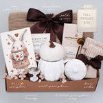 Gift box with various items including a pumpkin mug, boot socks, and a drink sampler on a light gray background.