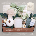 Gift box with various items including a mug, pumpkin, and candles on a neutral background.