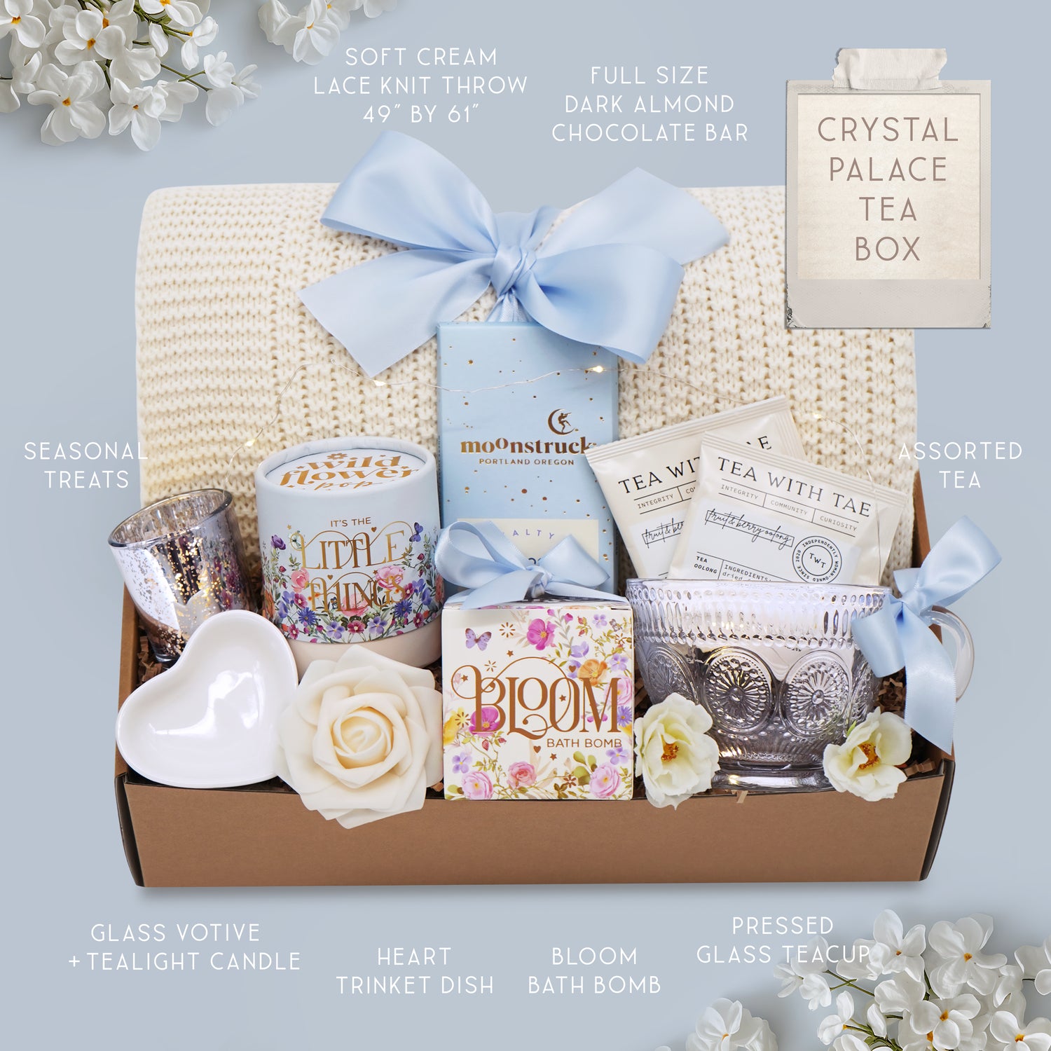 Cozy tea gift set with lace knit blanket, chocolates, bath bomb, and floral accents in soft blue packaging