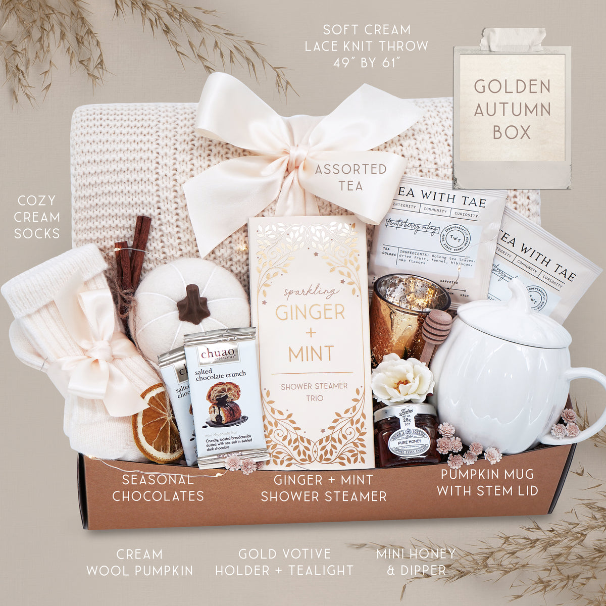 Golden Autumn blanket gift basket with tea, candles, and other items on a gray background