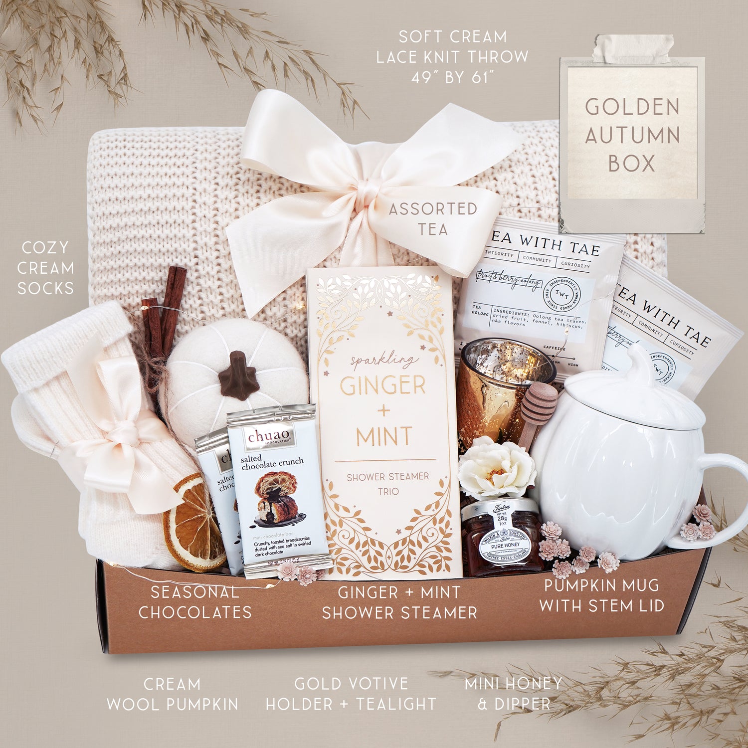 Golden Autumn blanket gift basket with tea, candles, and other items on a gray background