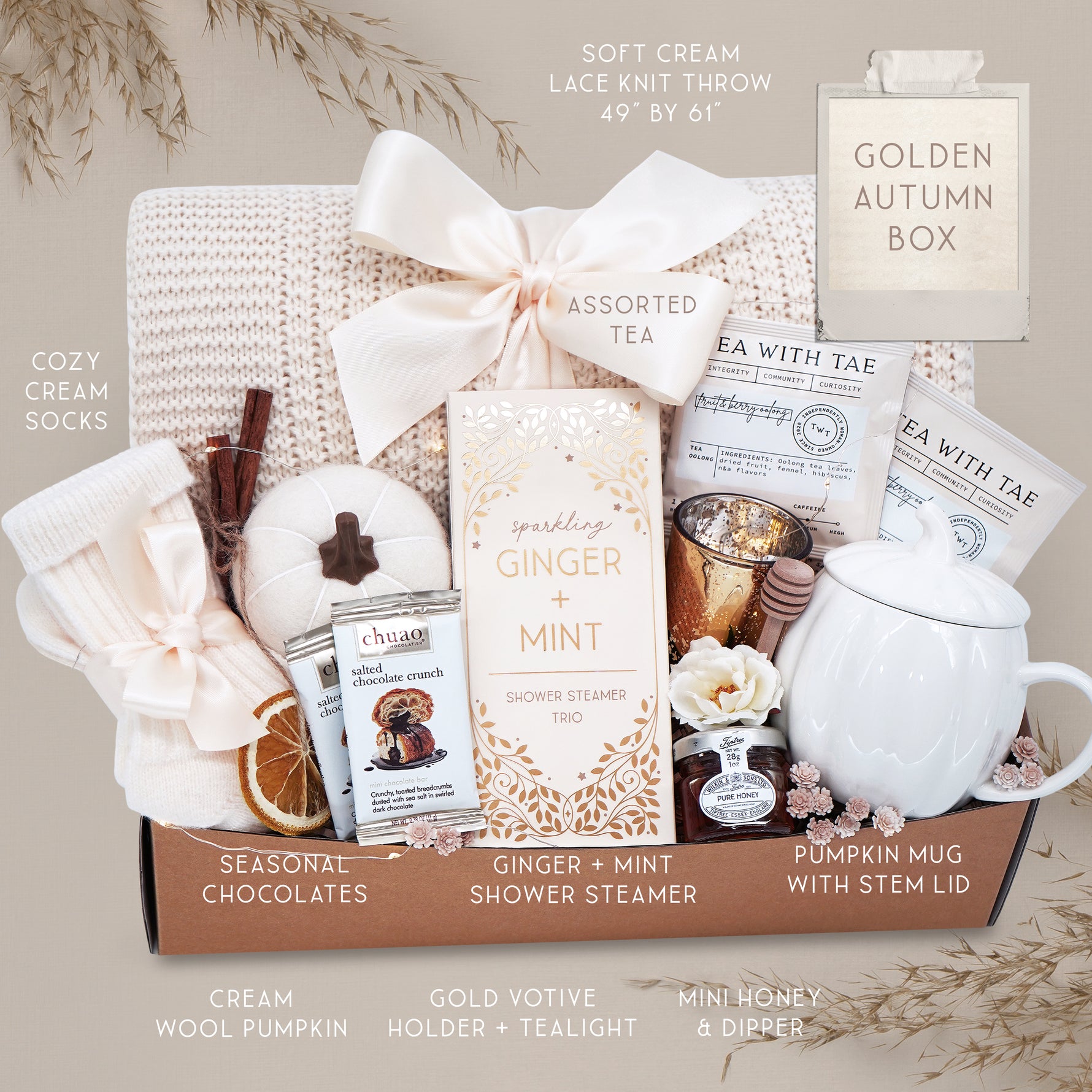 Golden Autumn blanket gift basket with tea, candles, and other items on a gray background