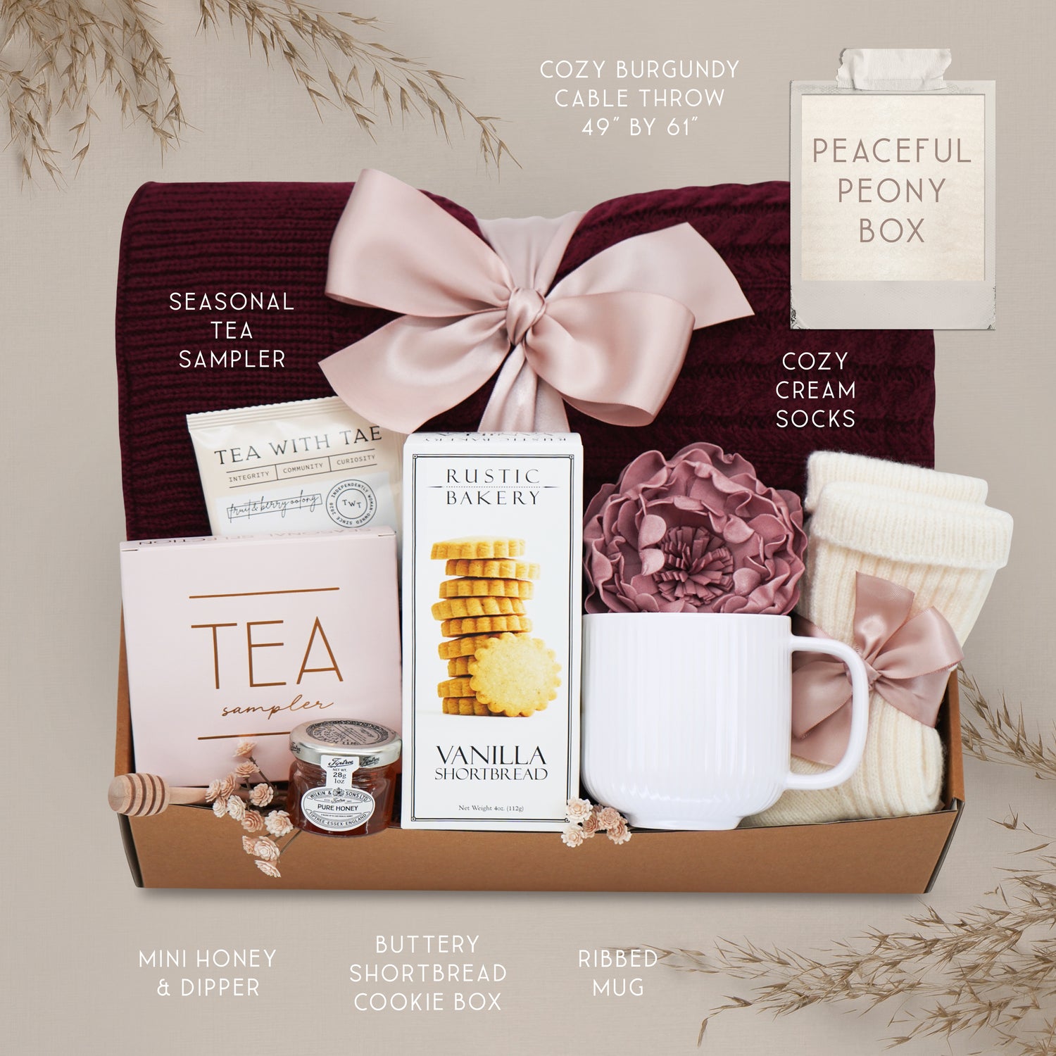 Peaceful Peony by Wildflower Pop comes with a Burgundy cable knit blanket, Rustic Bakery shortbread cookies, Tea Sampler, mini honey and dipper, cream ribbed ceramic mug, cream knit socks, and faux peony