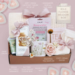 Wildflower Pop wildflower meadow blanket gift box with a cream lace knit blanket, Rosewater face mask, gold spoon, tea sampler, cream knit socks, faux rose, wildflower ceramic mug, wood butterfly ornament, Rustic bakery vanilla shortbread, Flower Market gardenia hand lotion 