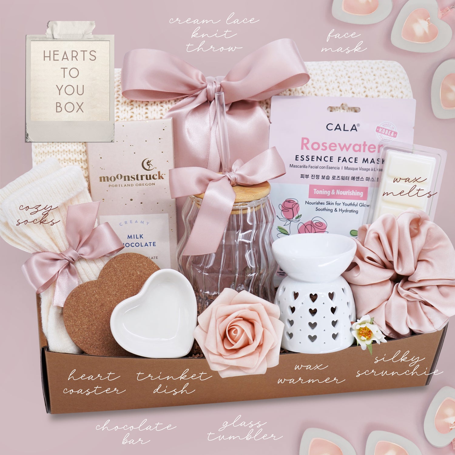 Gifting box with various items including a rosewater essence face mask, chocolate bar, and scented candle on a pink background.