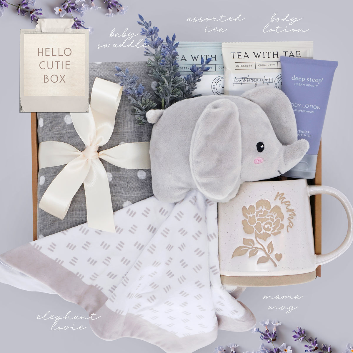 Baby gift set with elephant toy, mug, and swaddle blanket on a gray background.
