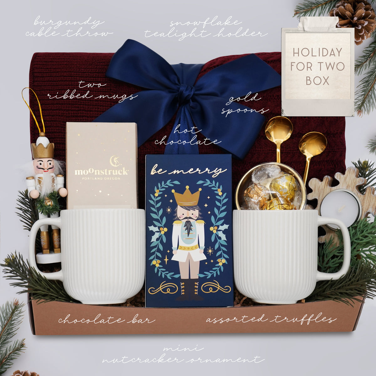 Wildflower Pop Holiday for Two Blanket Gift Box, with Burgundy cable knit blanket, chocolate bar, nutcracker ornament, drink sampler, truffle assortment, 2 gold demitasse spoons, 2 cream ceramic mugs, and snowflake votive 