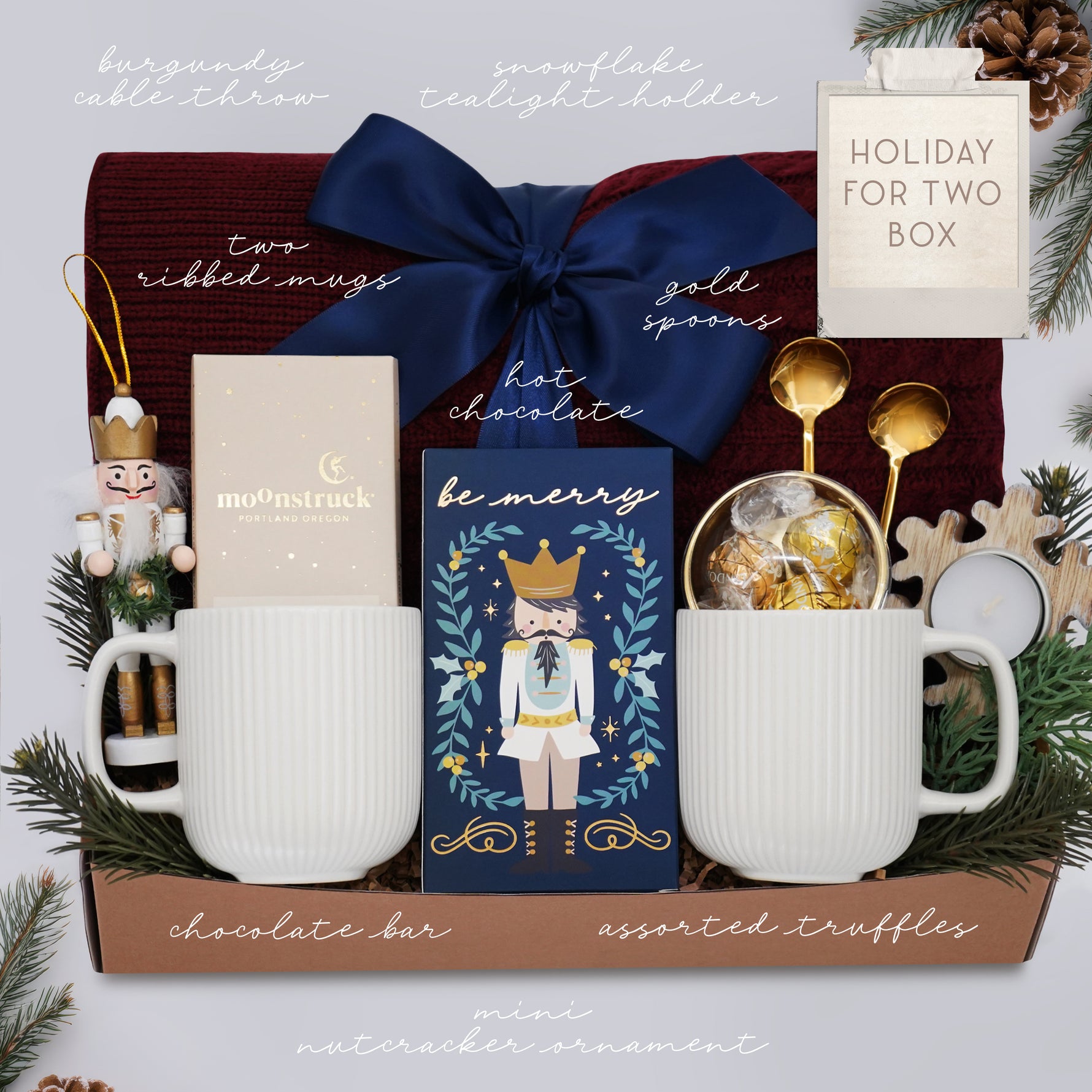 Wildflower Pop Holiday for Two Blanket Gift Box, with Burgundy cable knit blanket, chocolate bar, nutcracker ornament, drink sampler, truffle assortment, 2 gold demitasse spoons, 2 cream ceramic mugs, and snowflake votive 