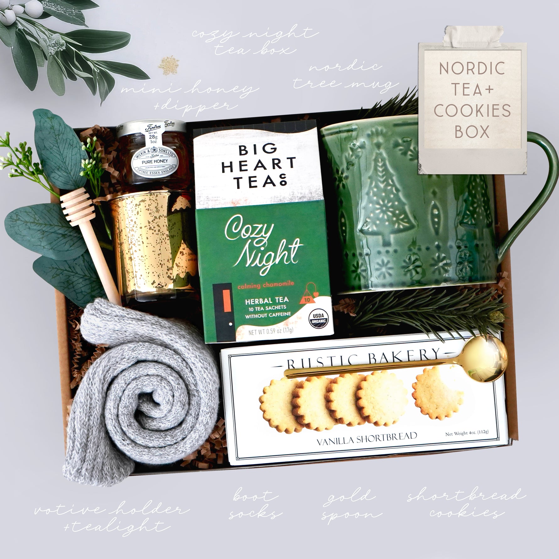 Wildflower Pop Gift set with a green mug, tea packaging, and cookies in a decorative box, grey cozy socks, gold votive, and mini honey and dipper on grey background