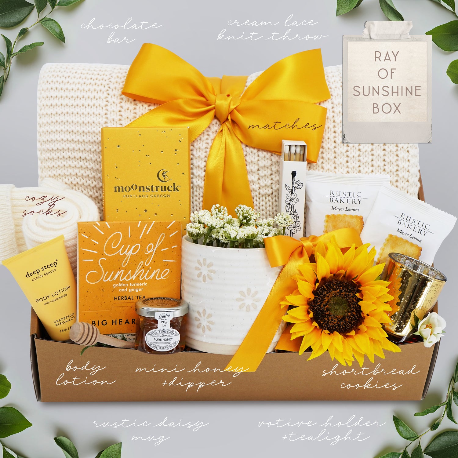 Gift box with various items including a sunflower, on a light gray background.