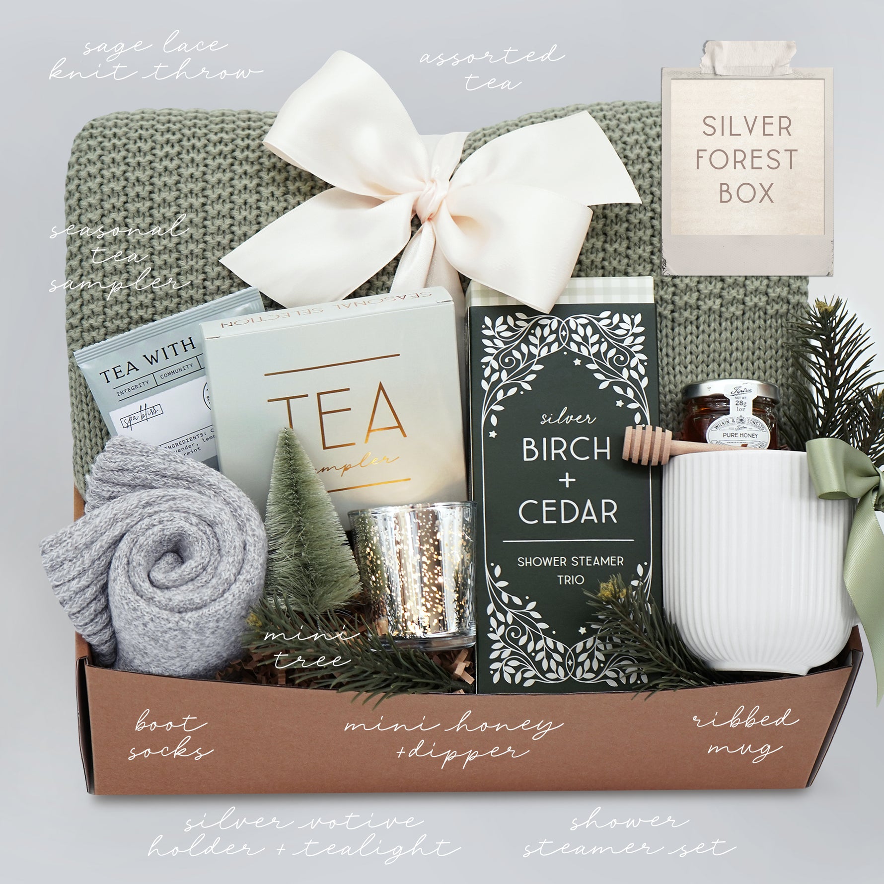 Wildflower Pop Silver Forest Blanket gift box, with sage green lace knit blanket, cream ribbed ceramic mug, grey cozy boot socks, silver votive and tea light, mini honey and dipper, silver birch and cedar shower steamers, and tea sampler