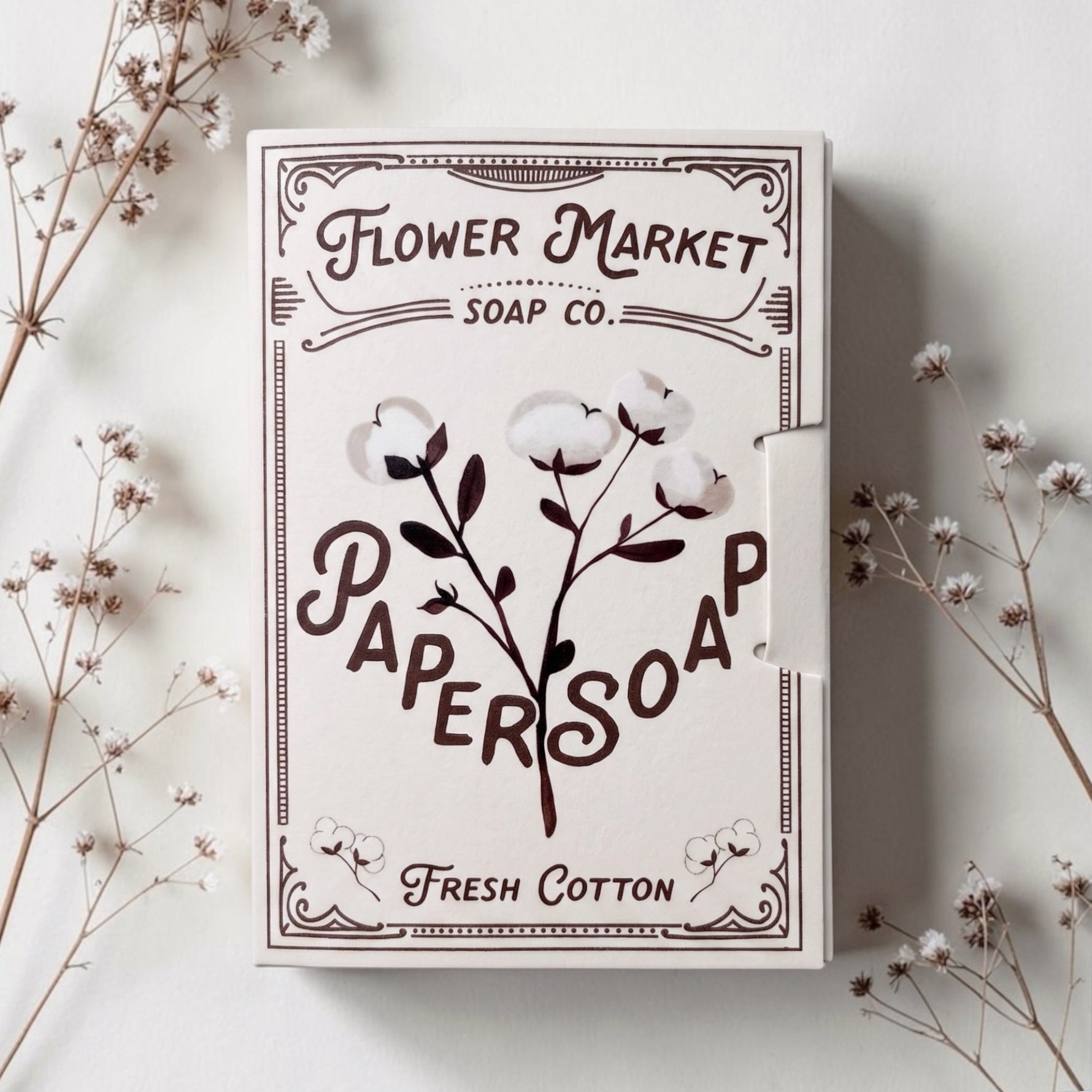 Flower Market Soap Co. Paper Soap in Fresh Cotton scent. Cream-colored packaging with dark brown typography and cotton illustrations, styled on a light surface with dried floral stems.