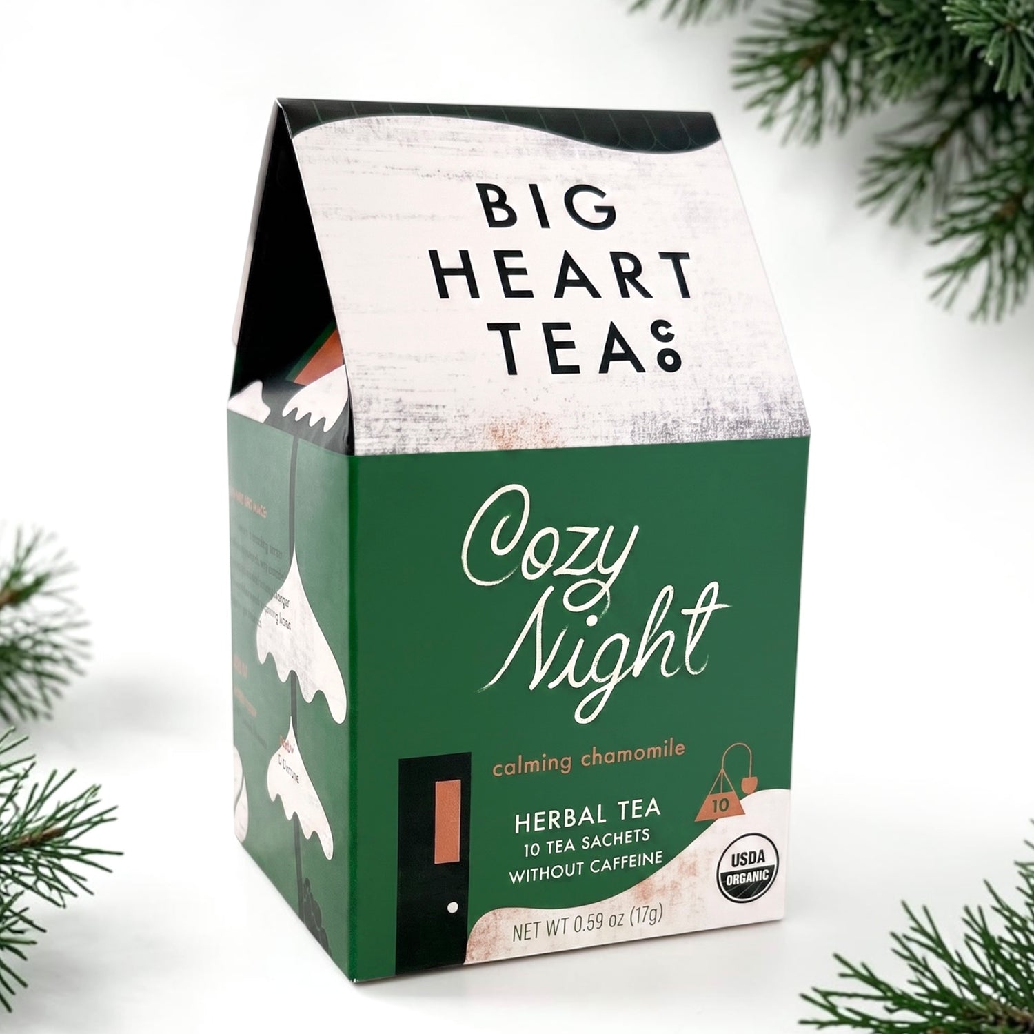 A box of Big Heart Teas Cozy Night herbal tea sachets, styled with pine branches on a white background.