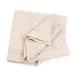A folded cream-colored lace knit blanket with textured patterns, shown on a solid white background.