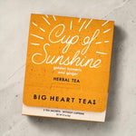 Orange packaging of 'Cup of Sunshine' herbal tea from Big Heart Teas on a light gray surface.