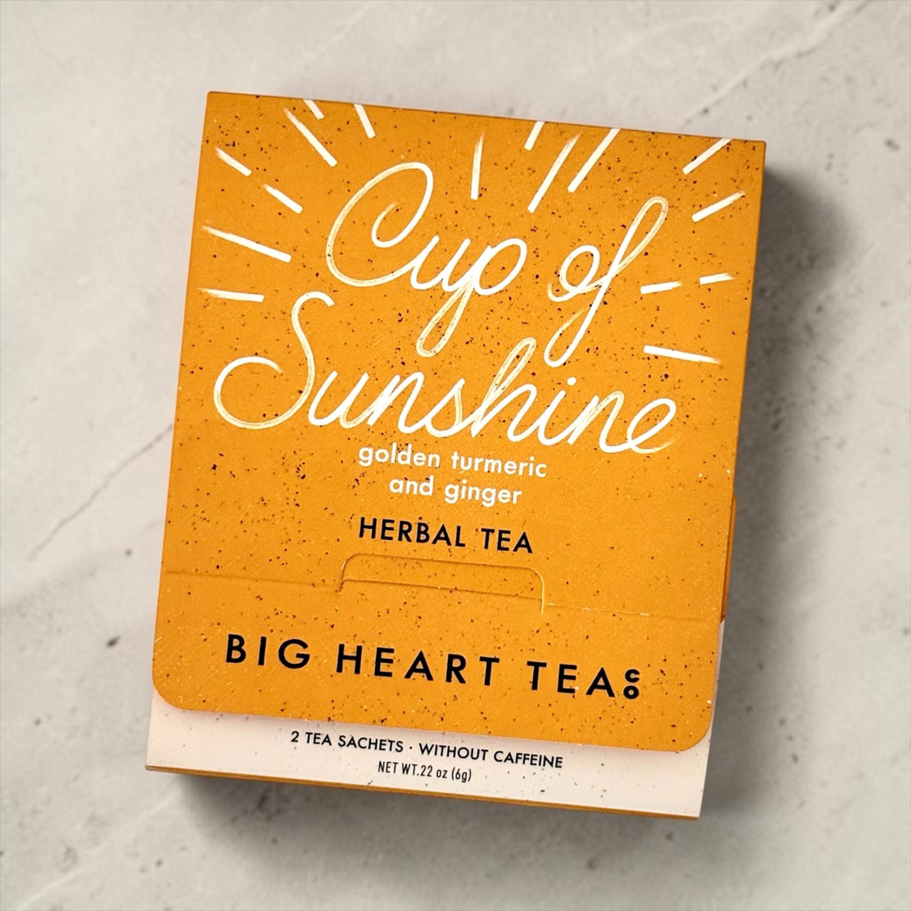 Orange packaging of 'Cup of Sunshine' herbal tea from Big Heart Teas on a light gray surface.