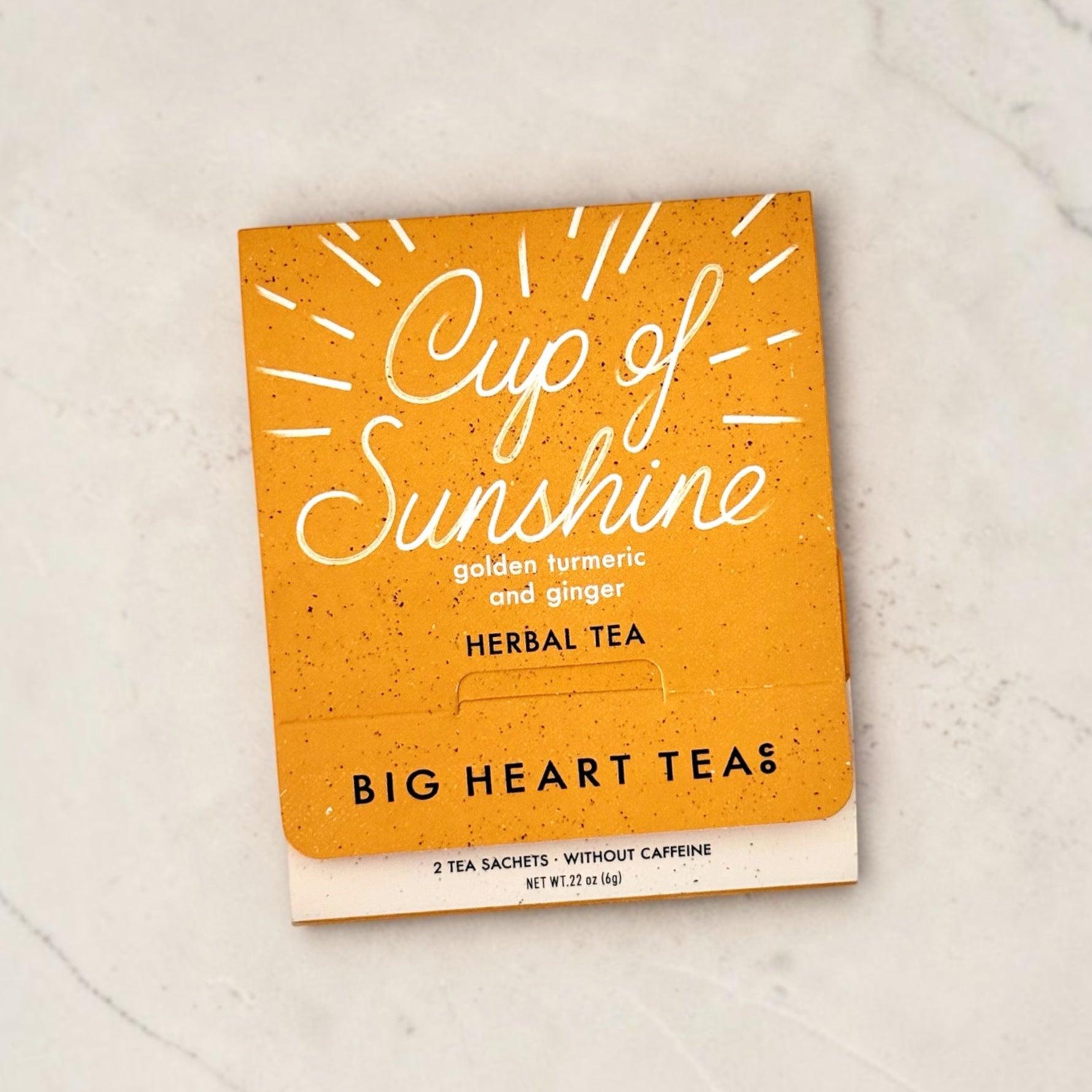 Orange packaging of 'Cup of Sunshine' herbal tea from Big Heart Teas on a light gray surface.