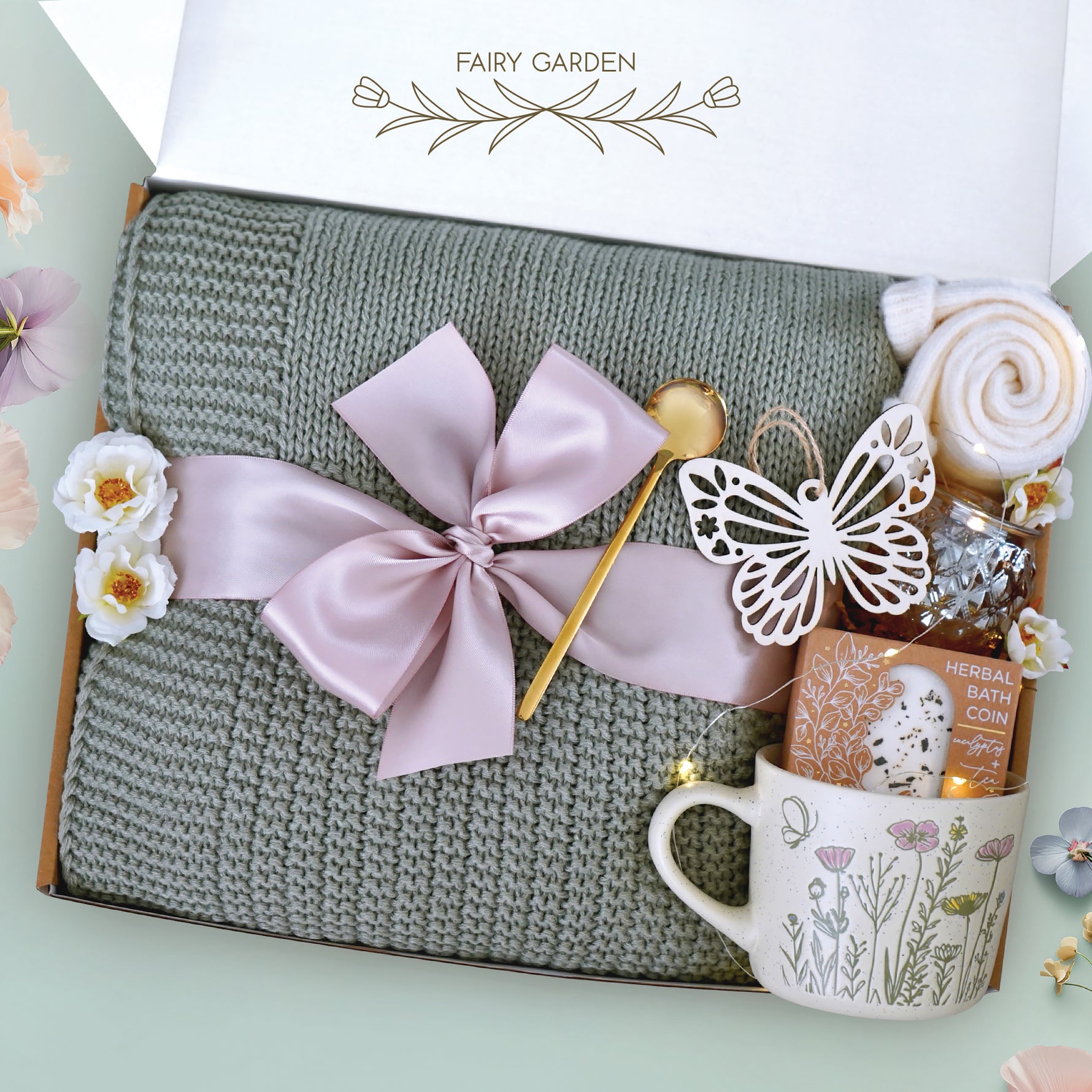 Our fairy garden blanket box comes with a sage green lace knit blanket, wildflower ceramic mug, votive and tea light, a string of fairy lights, cozy knit socks, a Wildflower Pop Eucalyptus and tea bath coin, wooden nordic butterfly ornament, and a gold demitasse spoon. The perfect gift for a beloved teacher helping your child grow. 