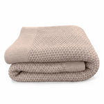 A folded honeycomb weave knit blanket in a warm taupe-beige color with a ribbed knit border, set against a plain white background.