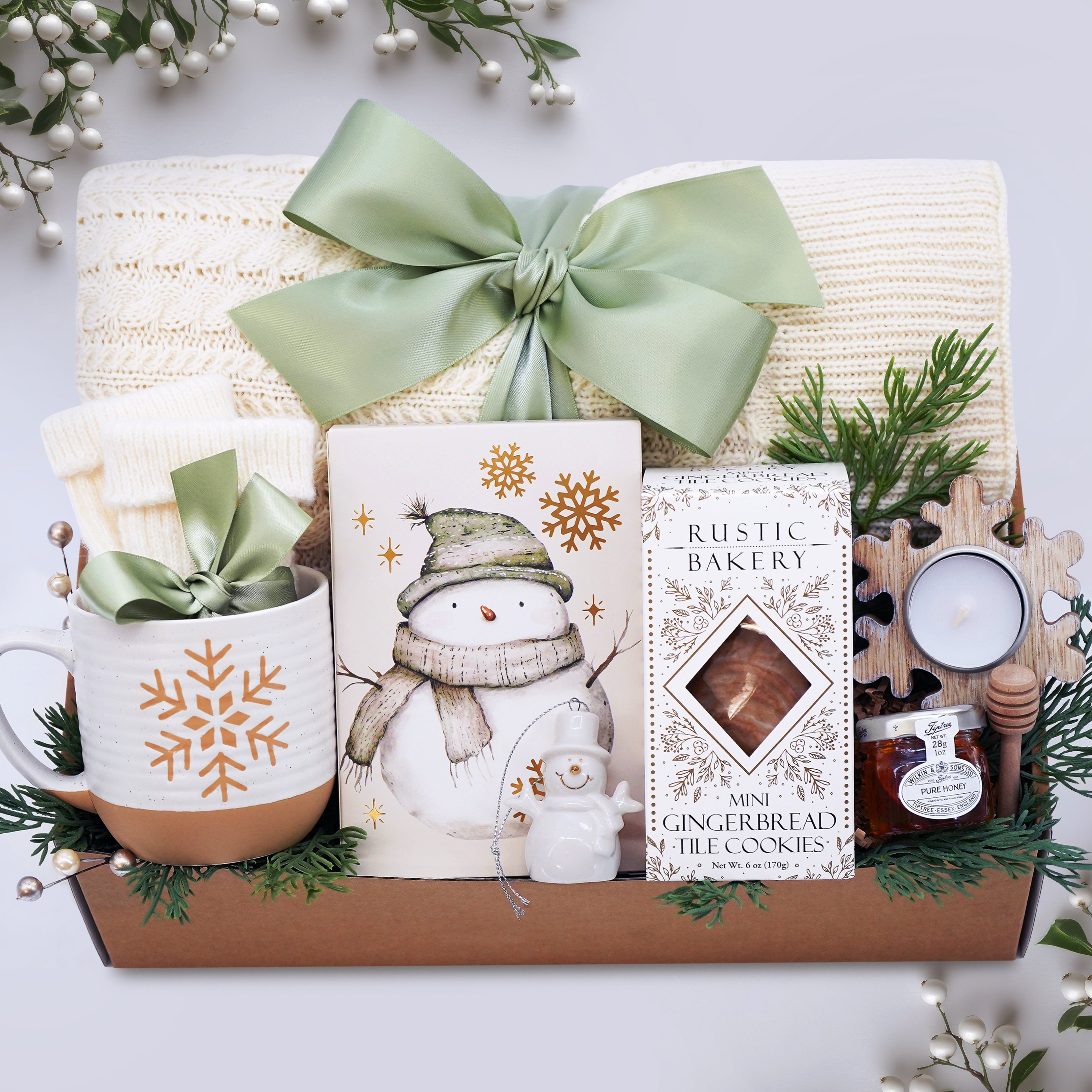 Wildflower Pop Frosty's Flurries Blanket Box with blanket, socks, Mini Gingerbread Cookies, drink sampler, ceramic snowman ornament, wooden snowflake votive and tea light, mini honey and dipper. 