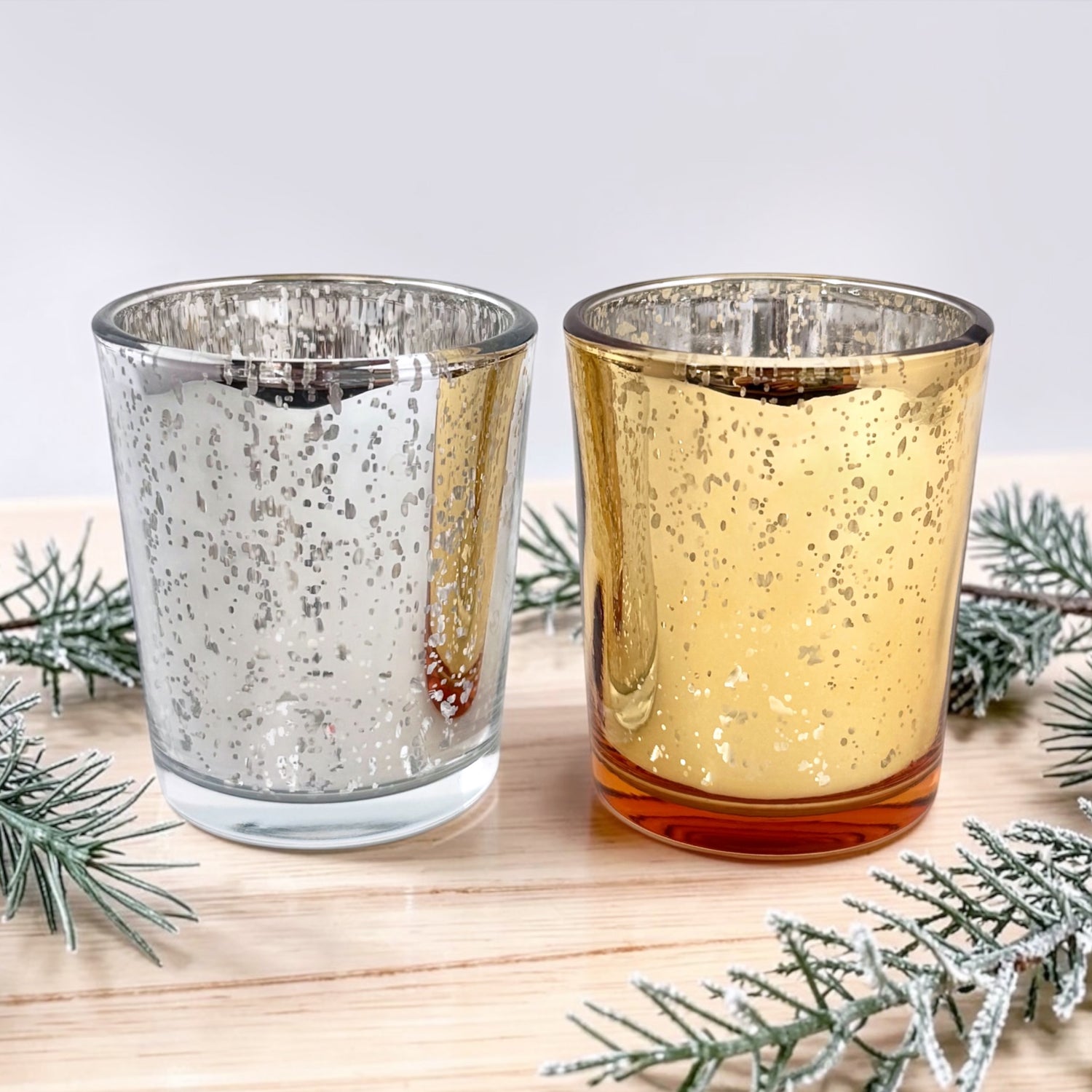 Silver and Gold Mercury Glass Votives on a light wood table with evergreen boughs 