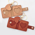 Small leather keychains with heart-shaped cutout picture frames and gold-tone key rings, shown on a light neutral background. Top is gold, bottom is reddish brown.