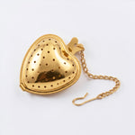 A gold-colored metal heart-shaped tea infuser with a matching chain, shown on a clean white background.
