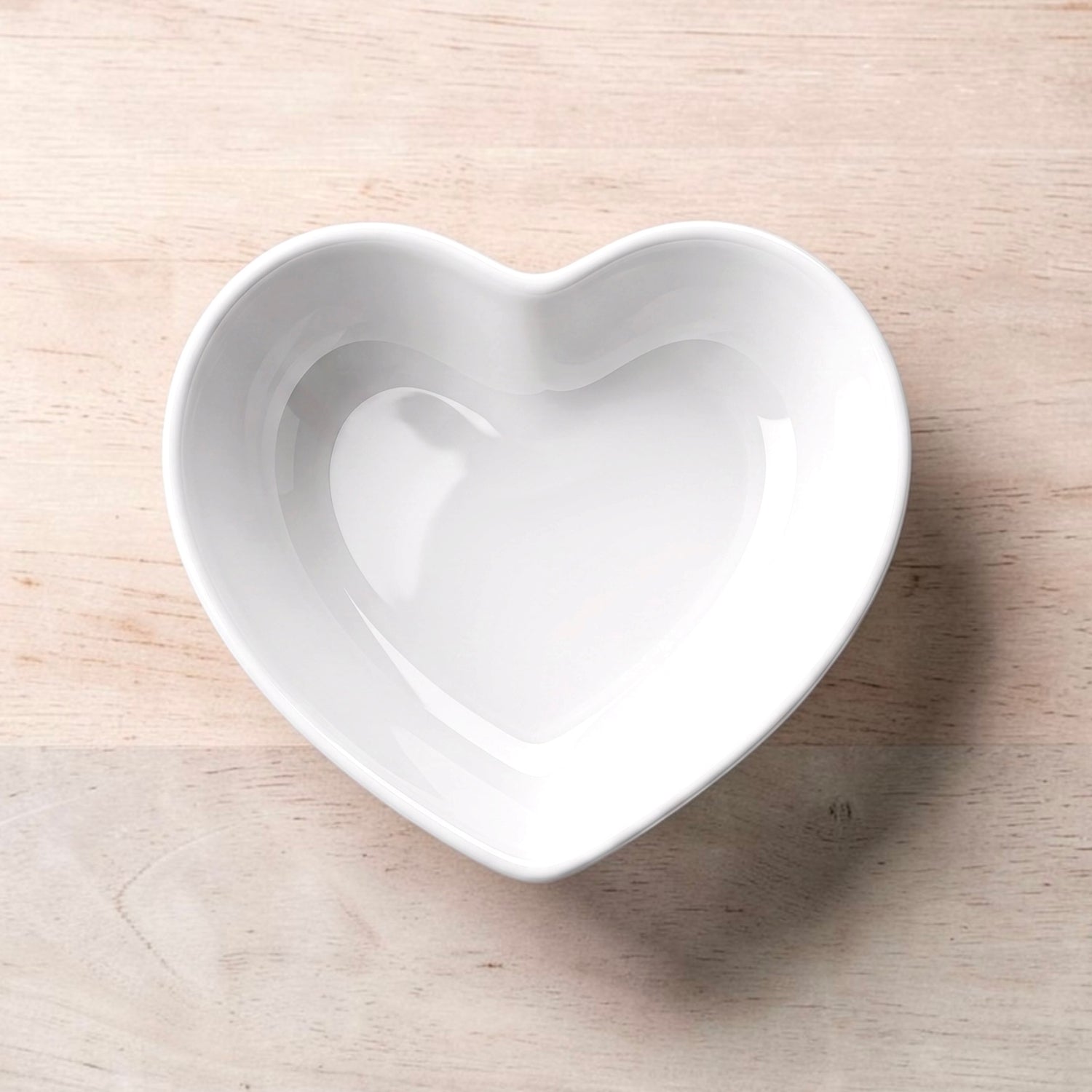 A white heart-shaped ceramic trinket dish placed on a light wood surface.