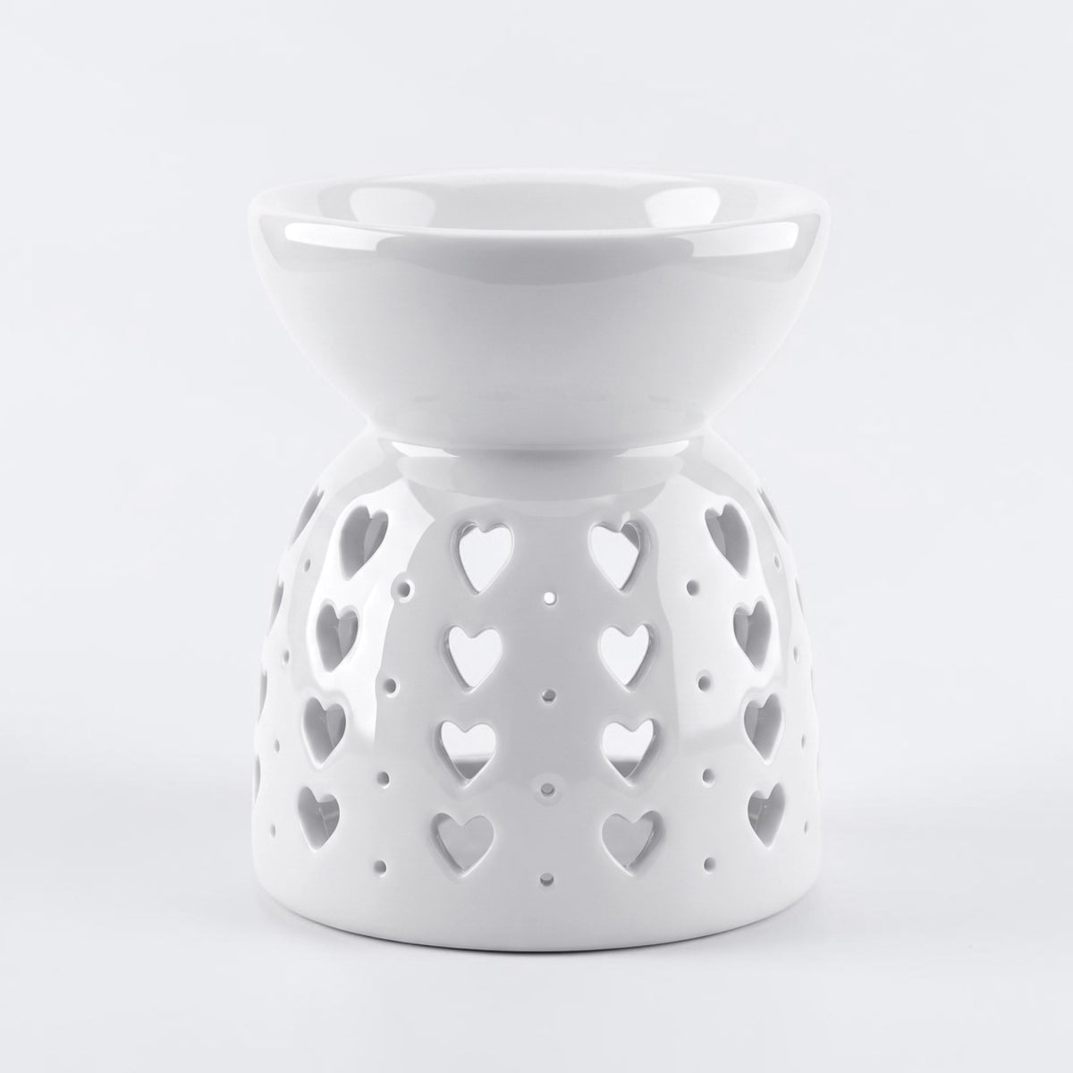 A white ceramic wax warmer/diffuser with a heart-shaped cutout pattern, set against a light gray background.