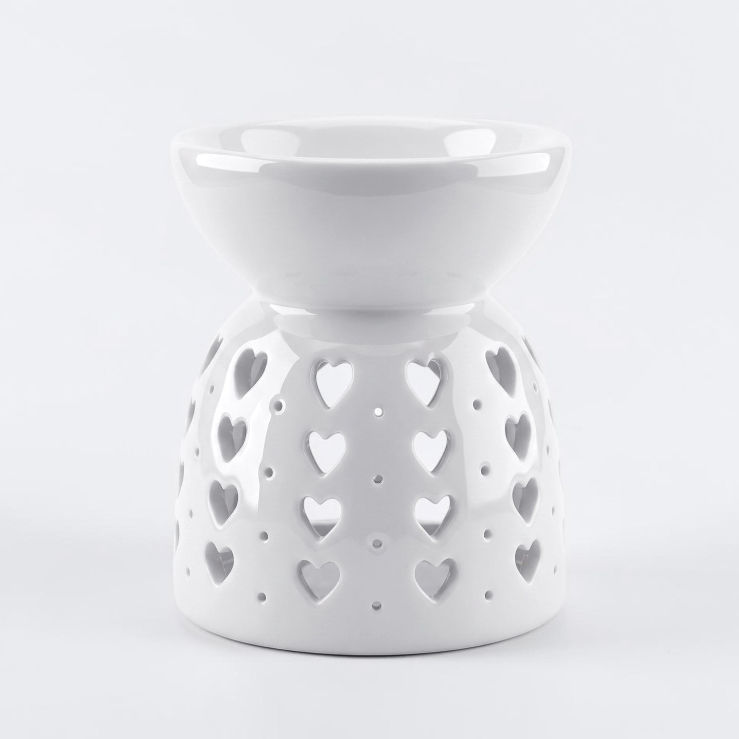 A white ceramic wax warmer/diffuser with a heart-shaped cutout pattern, set against a light gray background.