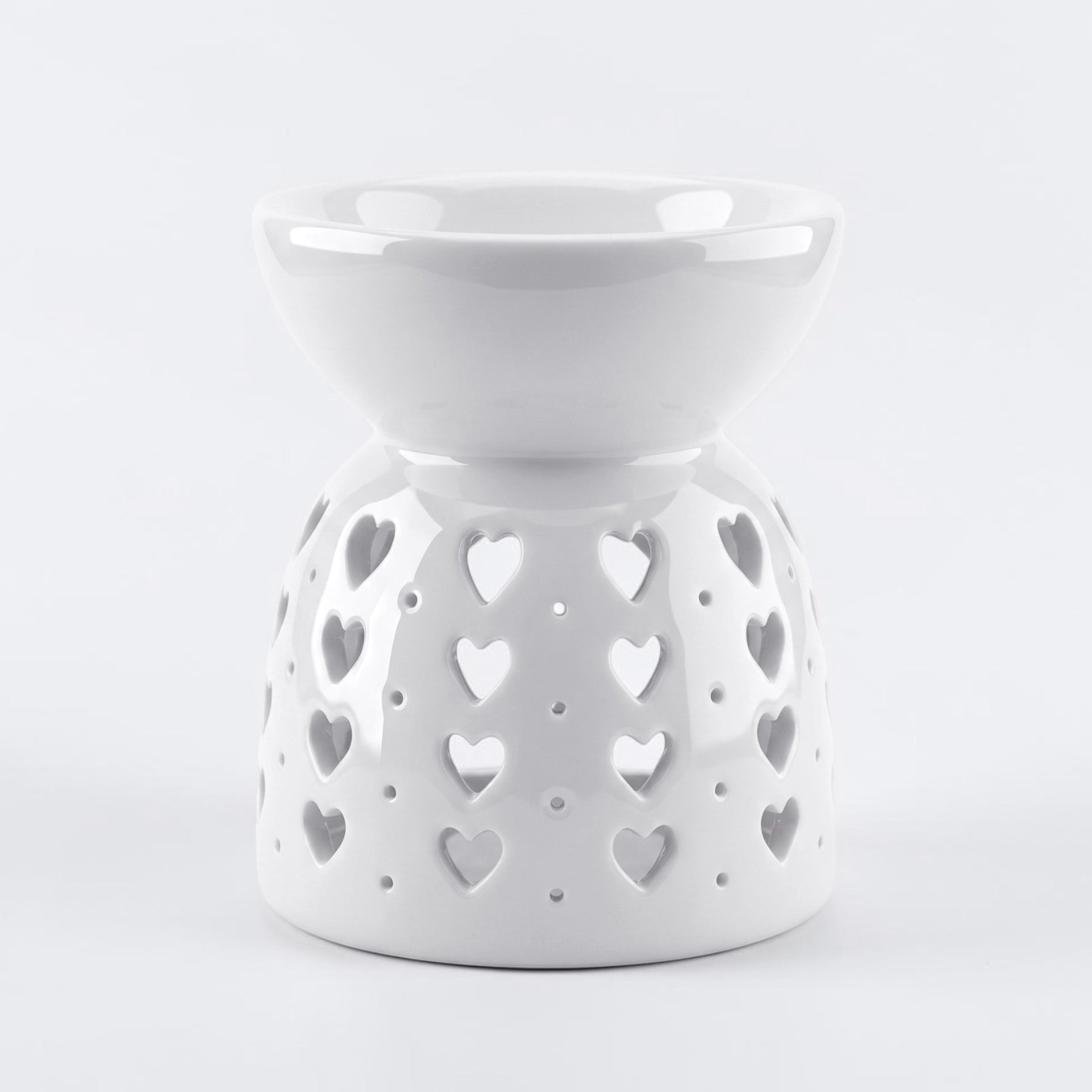 A white ceramic wax warmer/diffuser with a heart-shaped cutout pattern, set against a light gray background.