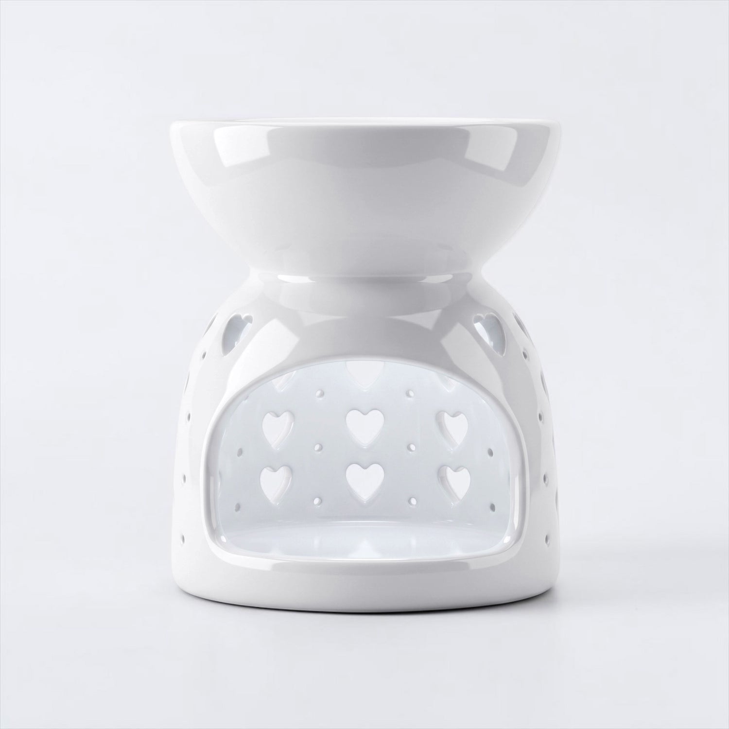 A white ceramic wax warmer/diffuser with a heart-shaped cutout pattern, set against a light gray background.