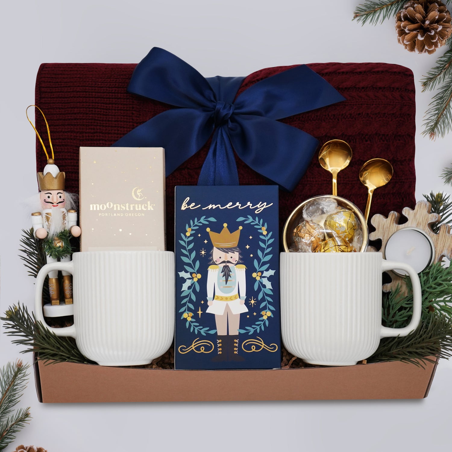 Wildflower Pop Holiday for Two Blanket Gift Box, with Burgundy cable knit blanket, chocolate bar, nutcracker ornament, drink sampler, truffle assortment, 2 gold demitasse spoons, 2 cream ceramic mugs, and snowflake votive 