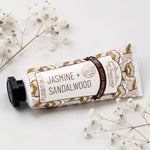 A tube of botanical scented Jasmine + Sandalwood hand cream by San Francisco Hand Cream, styled on a white background with dried flowers.
