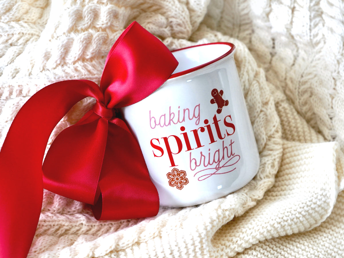Holiday mug is shown in a white ceramic with red rim with the saying baking spirits bright with a gingerbread man and a gingerbread snowflake 