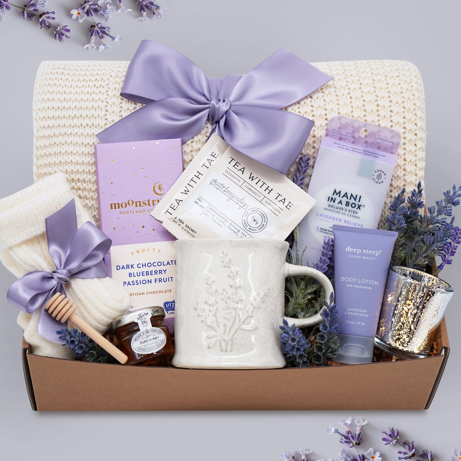 Gift basket with lavender-themed products including a mug, tea, and body lotion on a light gray background.