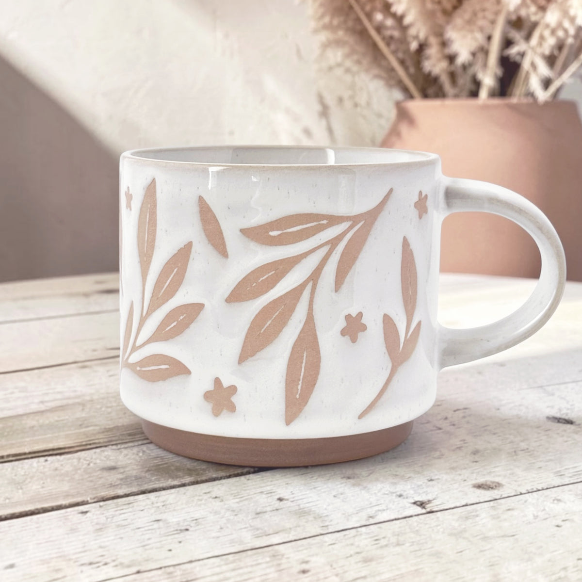 Ceramic mug with leaves and flower details on wood background