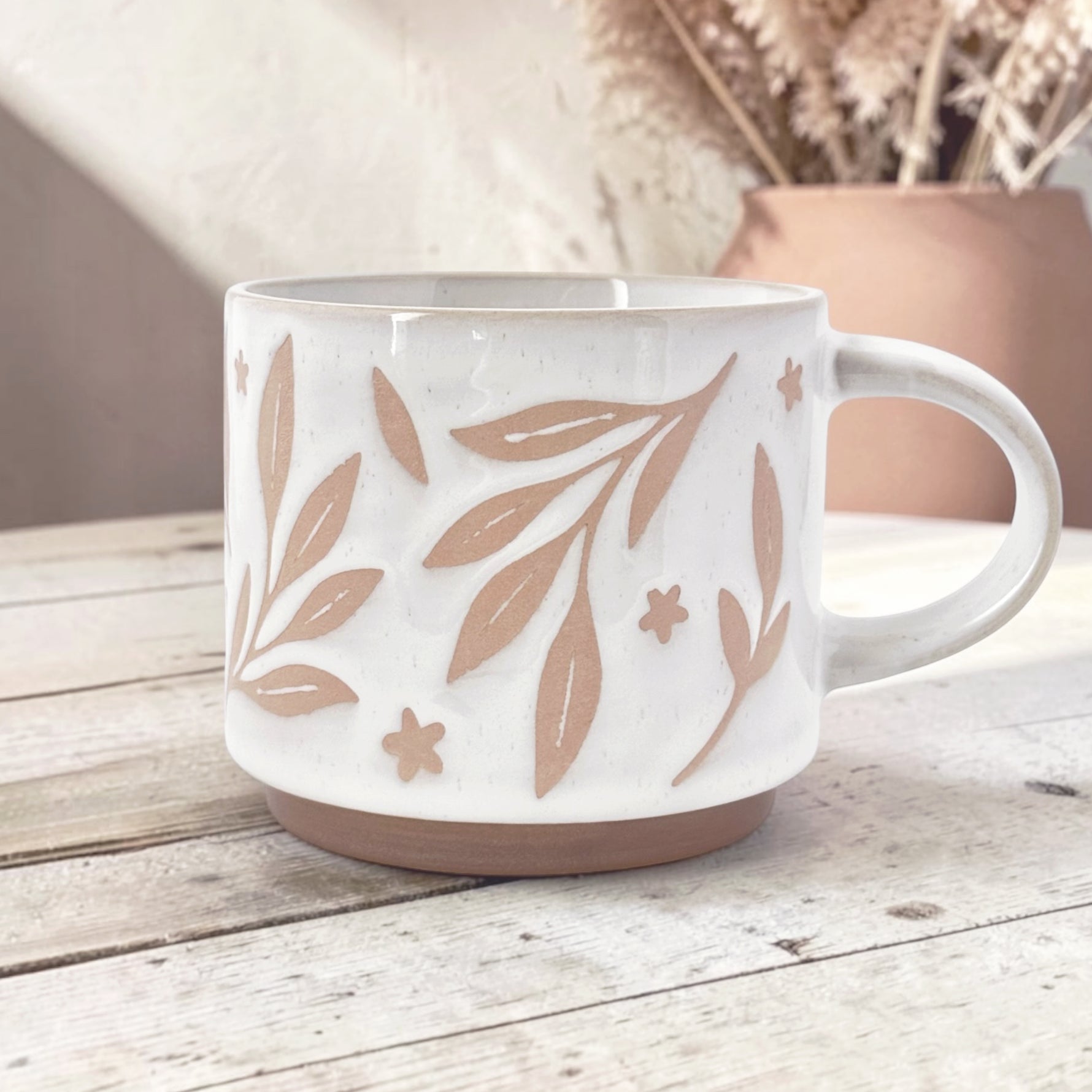 Ceramic mug with leaves and flower details on wood background