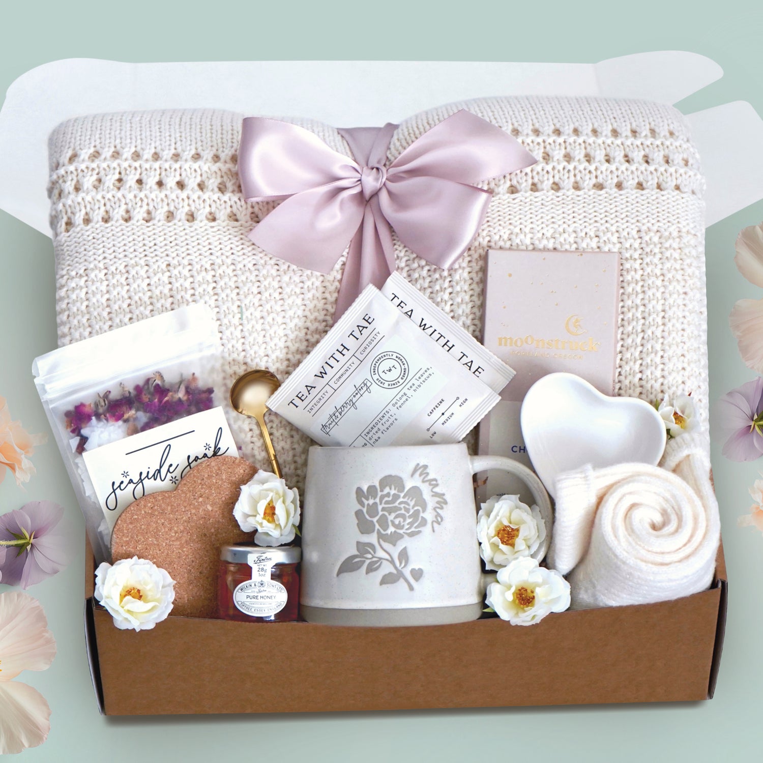 Love you mama blanket box comes with a cream lace knit blanket tied in a blush ribbon, 2 tea with tae tea bags, gold demitasse spoon, rose seaside soak bath salts, heart coaster, mini honey, mama ceramic mug, heart trinket dish, full size moonstruck milk chocolate bar, and cream knit socks